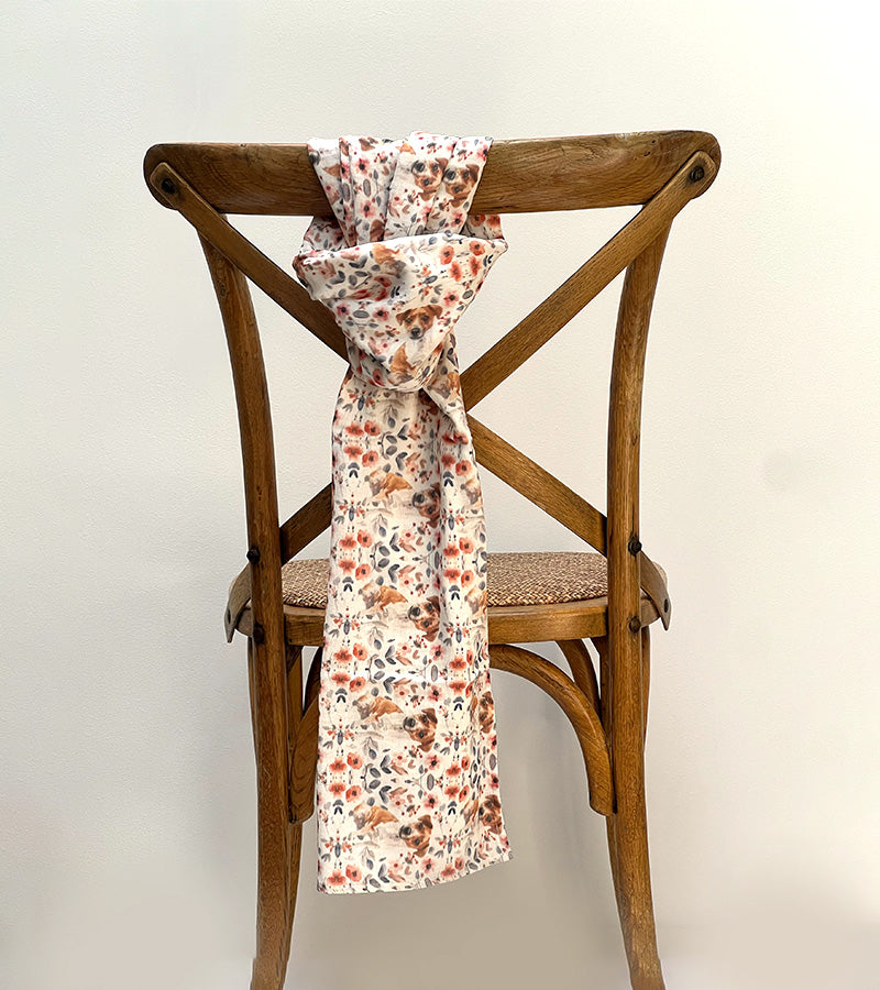 Floral-patterned and Jack Russell dog-patterned scarf draped over a wooden chair against a plain background