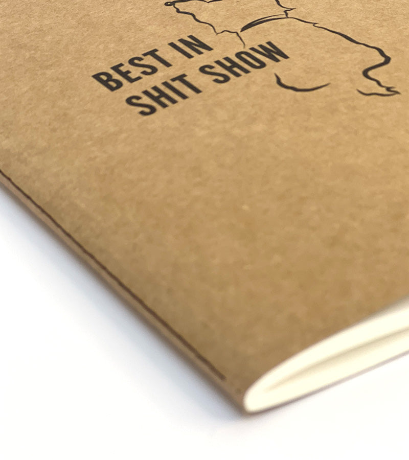 Brown notebook with 'Best in Shit Show' text and a dog illustration on a white background