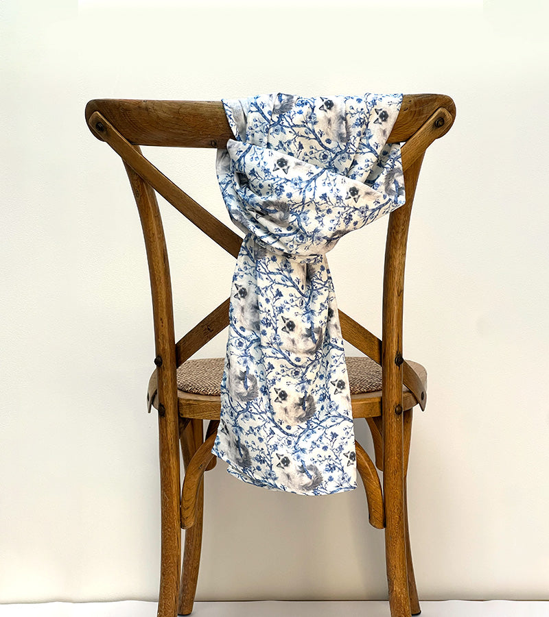 Blue floral patterned and Birman cat-patterned scarf draped over a wooden chair against a plain background