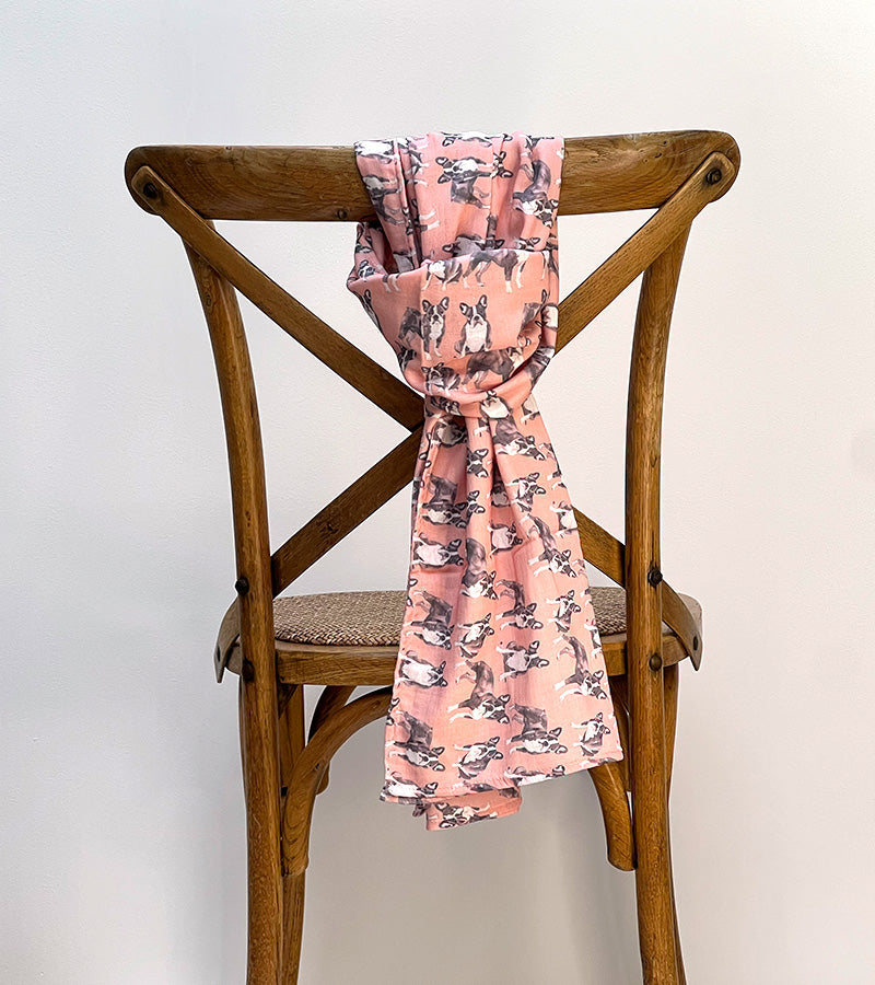 Coral scarf with Frenchie dog pattern draped over a wooden chair against a white background