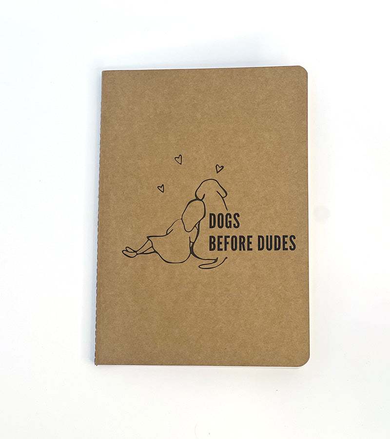 Brown paper notebook with a dog illustration and 'Dogs before dudes' text on a white background