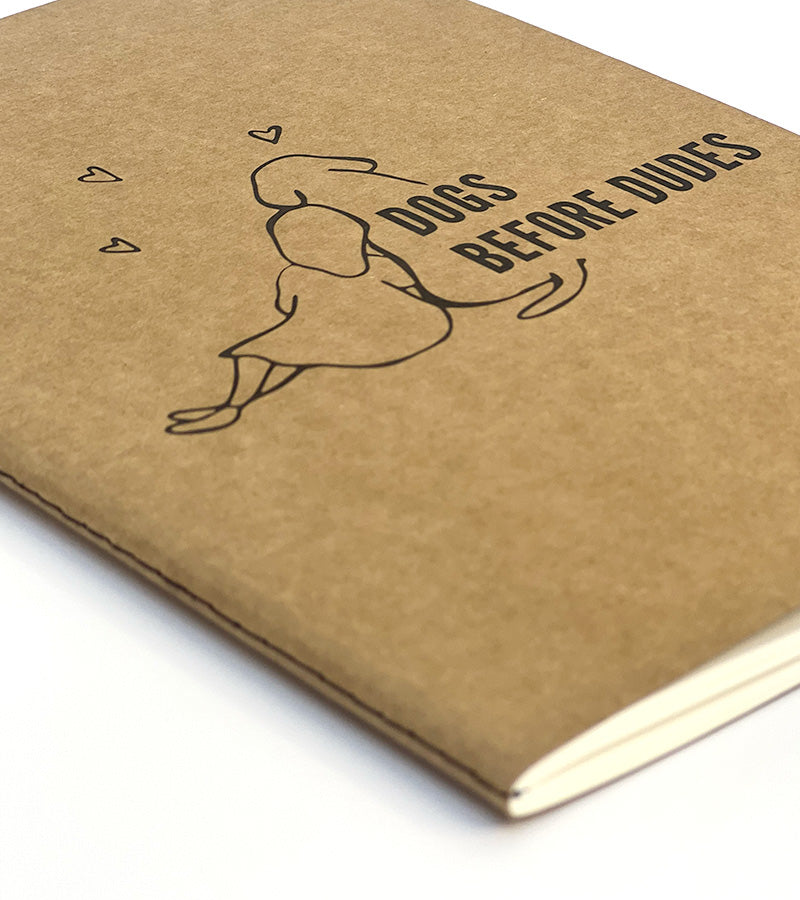 Brown paper notebook with a dog illustration and 'Dogs before dudes' text on a white background
