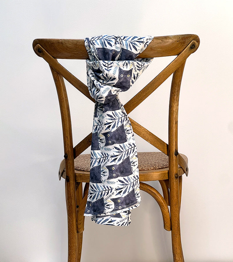 Scarf with black cat pattern draped over a wooden chair against a white background