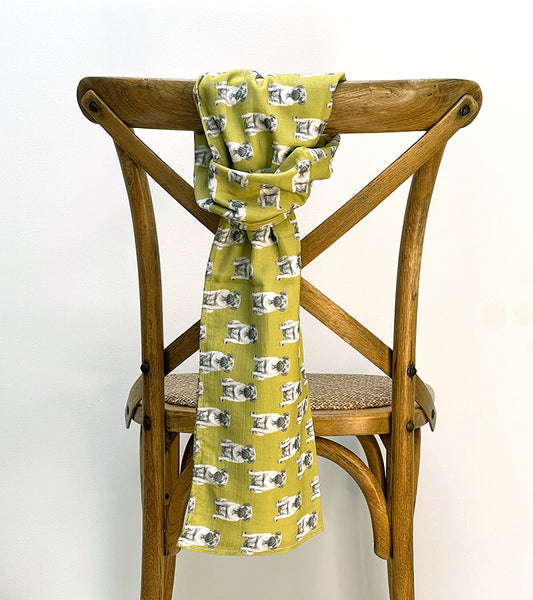 Green scarf with pattern of pugs draped over a wooden chair against a white background