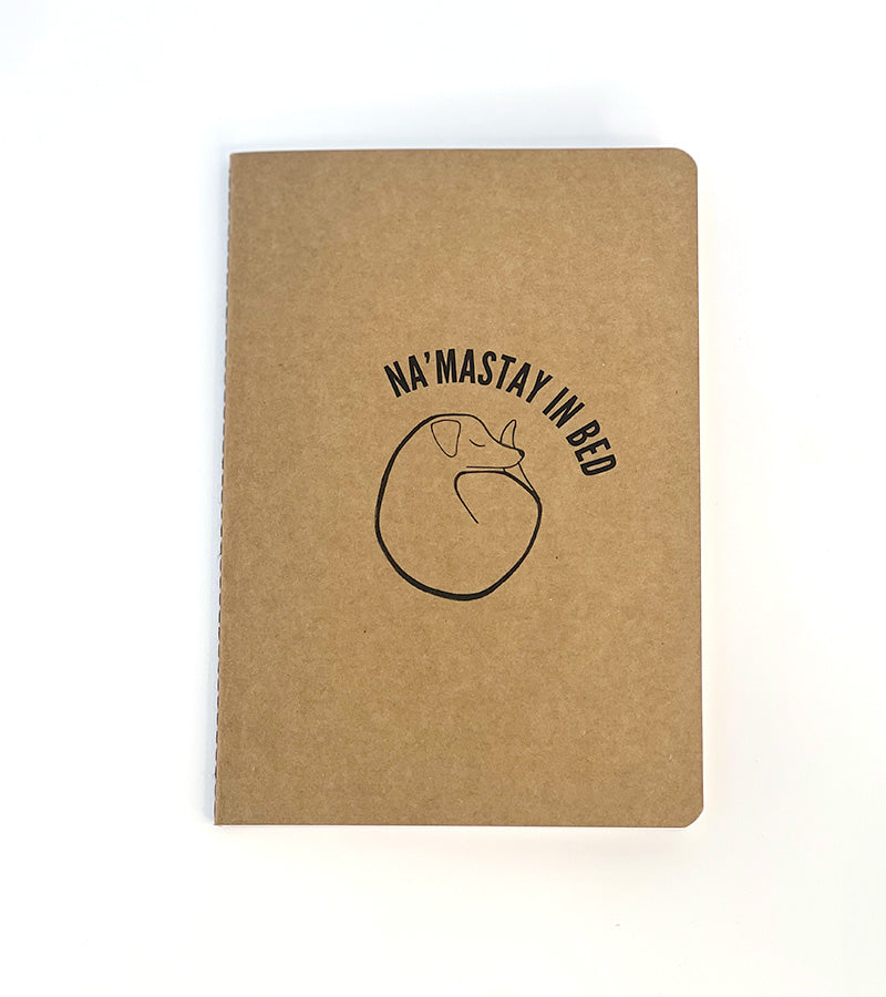 Brown notebook with 'Na'Mastay in Bed' text and dog sleeping illustration on a white background