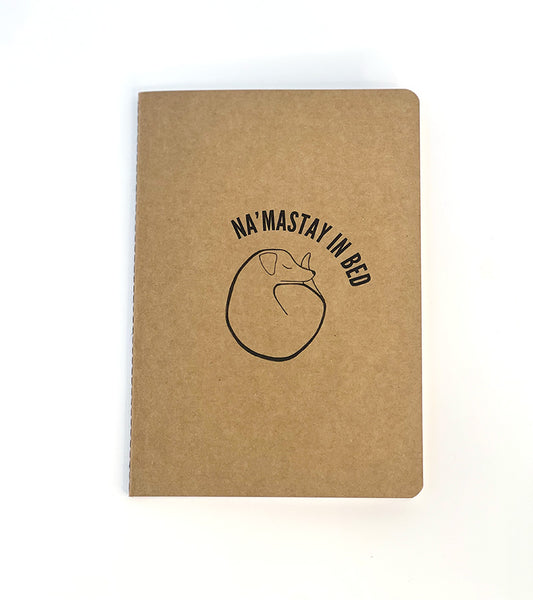 Brown notebook with 'Na'Mastay in Bed' text and dog sleeping illustration on a white background