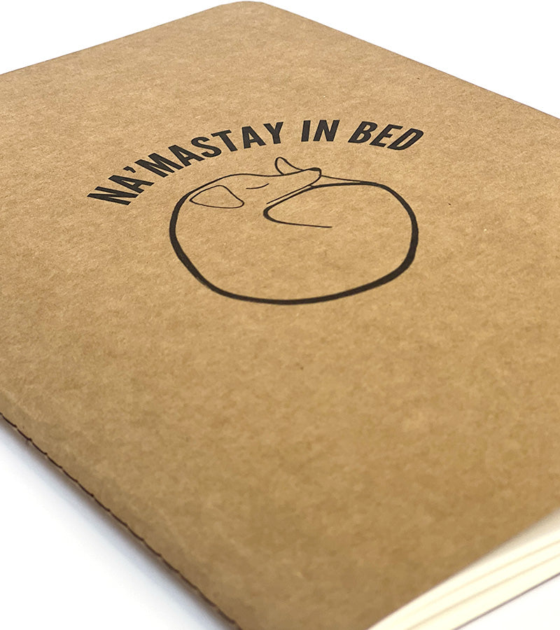 Brown notebook with 'NA'MASTAY IN BED' text and a sleeping cat illustration on a white background