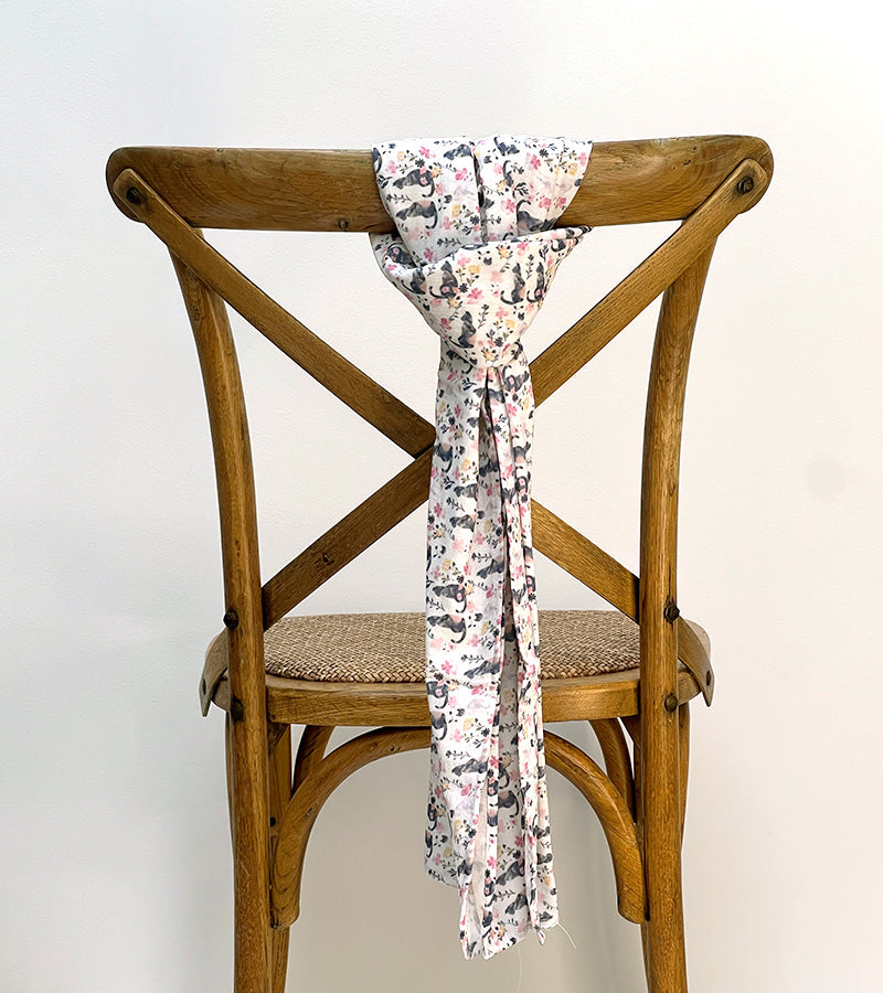 Scarf with a black cat and pink floral pattern draped over a wooden chair against a white background