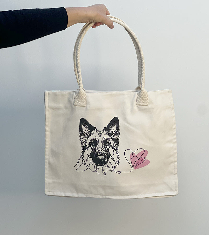 Tote bag with a German Shepherd dog illustration and pink hearts held by a hand against a plain background
