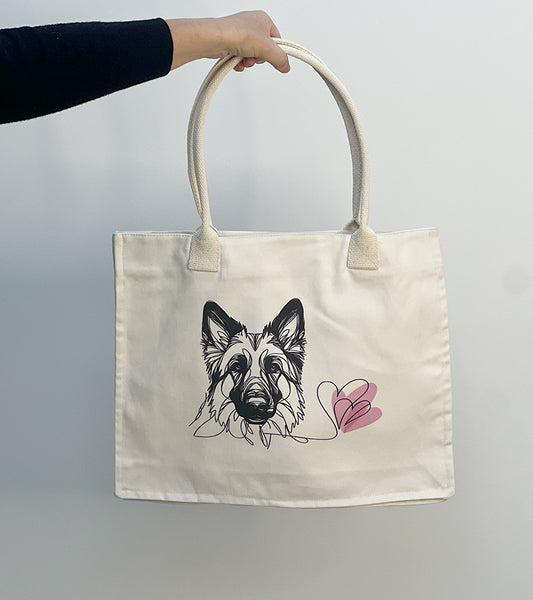 Tote bag with a German Shepherd dog illustration and pink hearts held by a hand against a plain background