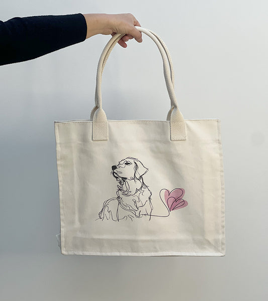 Tote bag with a Golden Retriever dog illustration and pink hearts held by a hand against a plain background