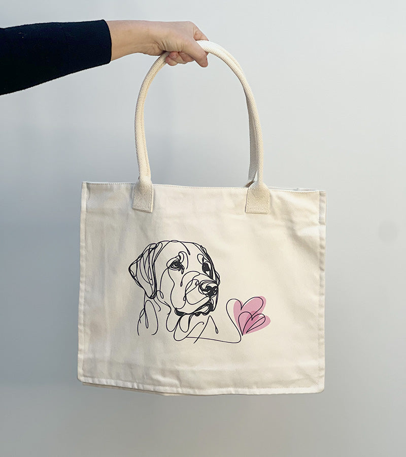 Tote bag with a Labrador dog illustration and pink hearts held by a hand against a plain background