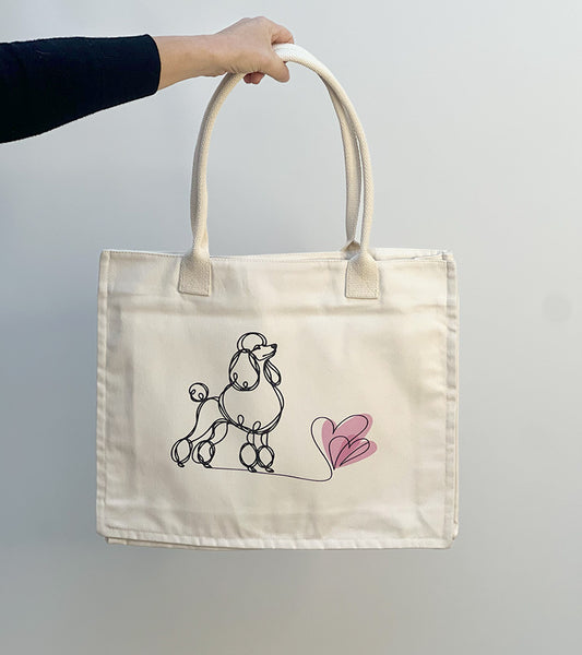 Tote bag with a Poodle dog illustration and pink hearts held by a hand against a plain background