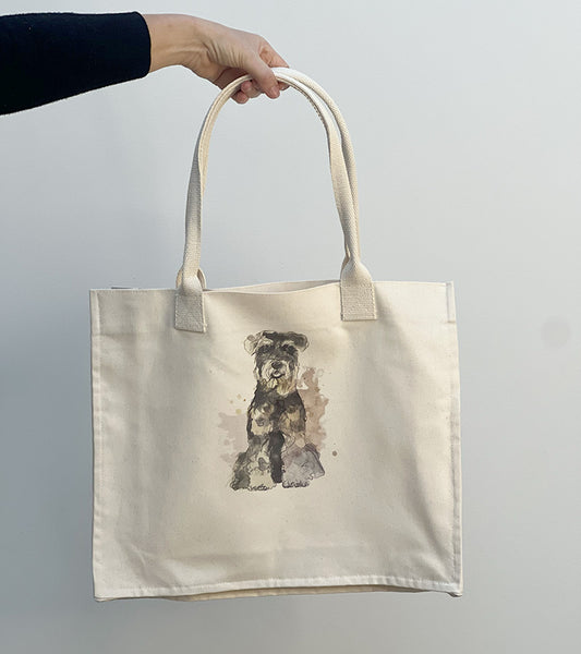Tote bag with a Schnauzer dog illustration and pink hearts held by a hand against a plain background