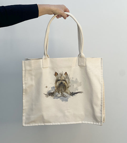 Tote bag with a Yorkie dog illustration held by a hand against a white background