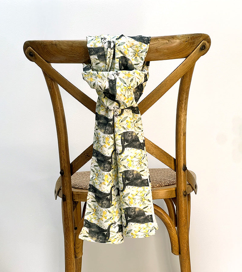 Scarf with a black cat and white/yellow floral pattern draped over a wooden chair against a white background